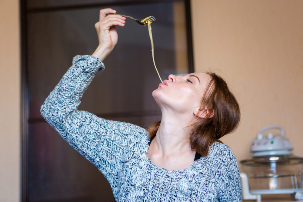 Amusing attractive young woman in grey knitted sweater  eating pasta in kitchen at home-1