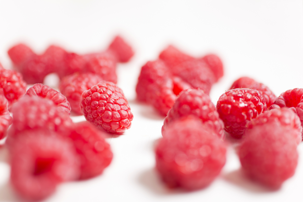Fresh red raspberries on a light wooden kitchen surface