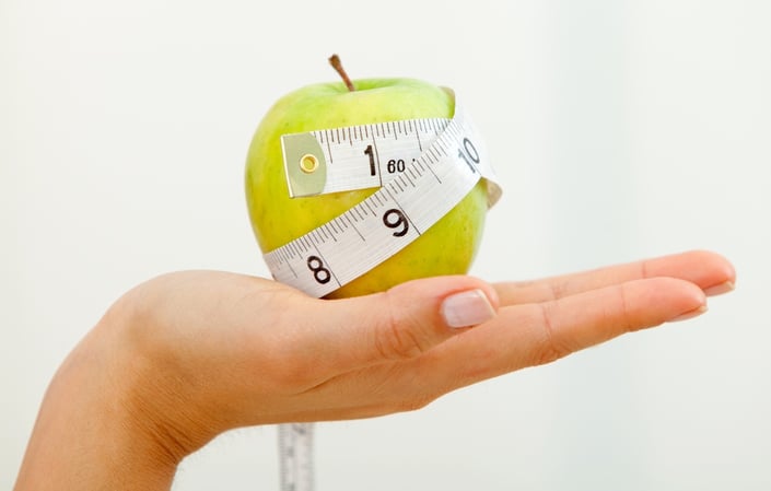 Hand holding an apple with a measuring tape around it isolated over a white background.jpeg