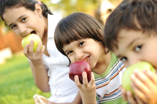 Small group of children eating apples together, shallow DOF