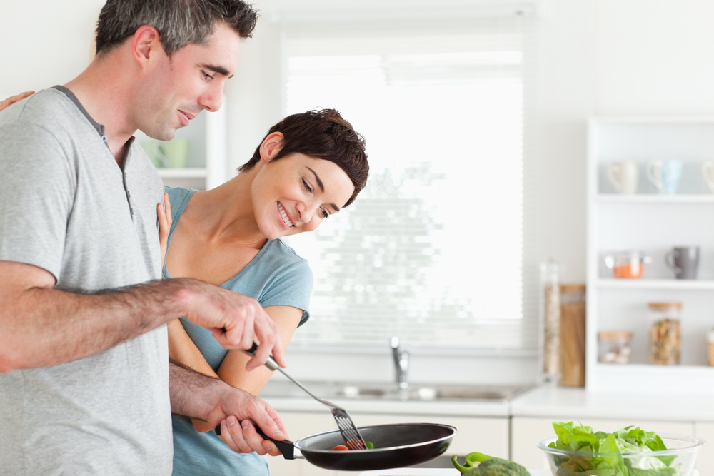 Woman looking into a pan her husband is holding in a kitchen