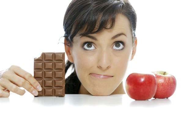 Young woman torn between a chocolate bar and fresh apple.jpeg